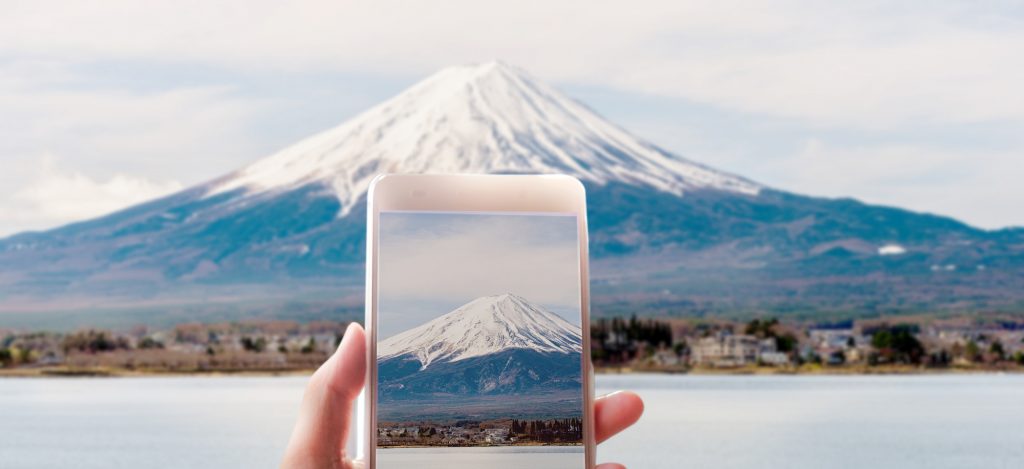 Hand of a woman taking a picture of Mount Fuji with a smart phone.